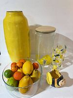 Group shot of all items: yellow vase, beverage dispenser, lemon glass, glass bowl with faux fruit, bee planter