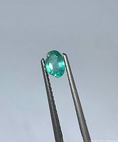 Emerald held in tweezers side view showing chip and colour
