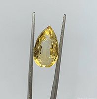 Pear cut light yellow citrine held by tweezers, full frontal view