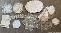 Group shot of all crochet lace doilies arranged on carpet showing variety of shapes, sizes and colors