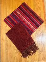 Both blankets displayed on hardwood floor: patterned kilim blanket and solid maroon throw