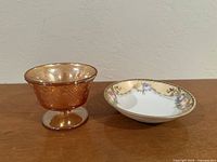 Footed marigold carnival glass sherbet beside floral porcelain bowl