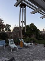 Large wood-topped wind chime with six metal tubes, wood striker and sail hanging from pergola in patio setting
