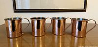 Four copper Moscow Mule cups lined up showing front view
