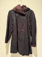 Full view of black side of reversible coat hanging, showing button and collar