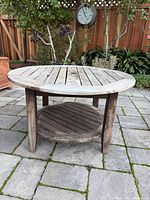 Full view of weathered round teak table on patio
