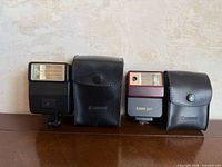 Two Canon flashes and two leather cases lined side by side