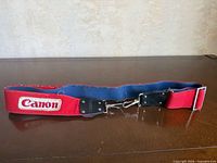 Full view of red Canon shoulder strap laid flat