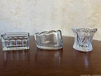 Front view of three clear pressed glass spoon rests on wood surface