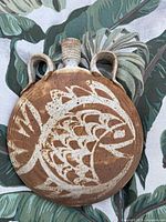 Front view of round stoneware vase showing fish motif and handles