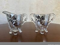 Front view of creamer and sugar bowl showing silver overlay and footed bases