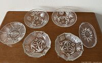 Six clear pressed glass dishes on wooden surface