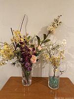 Two clear glass vases with faux flower arrangements on table