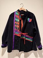 Full front view of black jacket with colorful appliqué and tie belt on hanger
