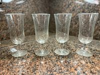 Four clear tulip-style wine glasses lined up on countertop