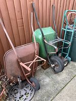 Overview of both wheelbarrows, hand truck and umbrella base against fence