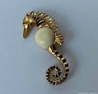 Front view showing gold seahorse form, cream cabochon belly, overall design