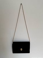Front view of black velvet Pourchet clutch hanging from gold-tone chain