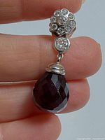 close view of one earring showing diamond cluster, bezel-set diamond, and faceted garnet drop