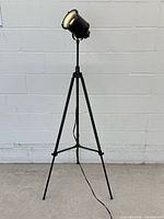 Full view of black metal tripod floor lamp with spotlight head and power cord