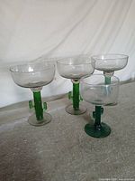 Four cocktail glasses with green cactus stems on tabletop