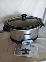 Full view of Hamilton Beach stainless steel slow cooker with glass lid and manual