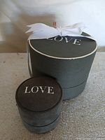 Two grey cylindrical boxes marked LOVE, white ribbon on larger