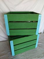 Two stacked green wooden crates with blue corner braces