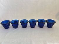 Six cobalt blue glass votive holders in a row—four smooth, two basketweave.