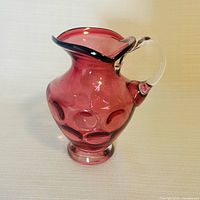 Front left view showing cranberry glass body, coin dot pattern, clear handle