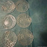 Six clear pressed glass grape motif plates laid out