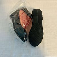 One shoe in protective plastic next to unpackaged shoe showing style and material