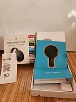 Front of retail box with Chromecast shown, open inner tray with device, setup insert visible