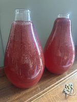 Two red bubble glass vases on wooden surface