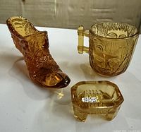 All three amber glass pieces—slipper, face cup, salt cellar—grouped