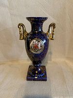 Front view showing cobalt urn, gold handles, medallion, pedestal base