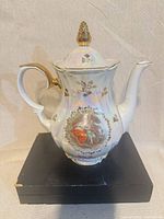Front view of Kahla porcelain coffee / teapot with lid, showing Rococo scene and gold trim