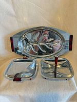 Front view of oval tray and two square dishes showing chrome finish and red Bakelite accents