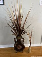Large and small brown/gold decorative vases with their stem arrangements against wall