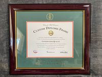 Front view of diploma frame showing dark wood, gold lip, green mat, university seal and text