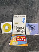 Group shot of all four items: Windows & MS-DOS 6.2 guide, Works & Encarta booklet, yellow Microsoft CD, Arthur’s Reading sleeve