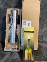 Electric wine opener packaged in cardboard insert beside Oster box and separate retail box containing wine chiller stick