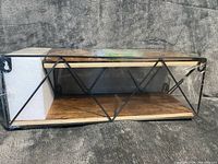 Wood shelf inside shrink wrap showing black metal frame with diamond pattern and mounting keyholes