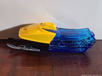 Left side view of cobalt blue glass snowmobile decanter with yellow plastic hood and black skis