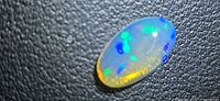 Oval cabochon crystal opal on textured background displaying multi-color play