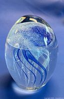 Front view of clear egg-shaped glass paperweight with blue jellyfish inside