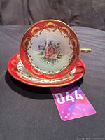 Teacup resting on saucer showing burgundy ground, gold filigree and rose motif