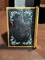 Front lid showing black enamel floral design and brass frame