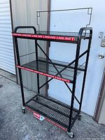 Front view of black metal Coca-Cola display cart showing three shelves and sign frame