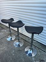Three black vinyl bar stools with chrome pedestal bases lined up outdoors